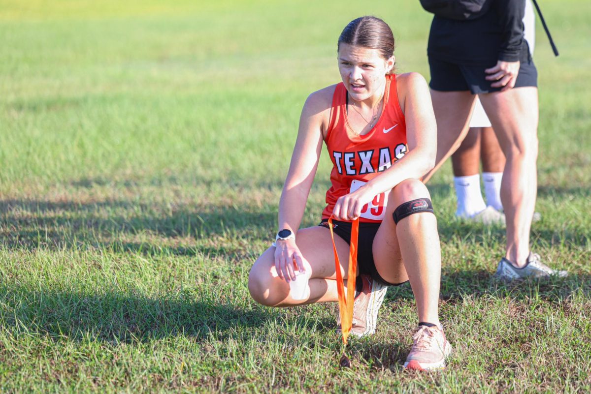 Junior Catie Loomis kneels with medal after crossing the finish line during Texas High's home Cross Country meet.